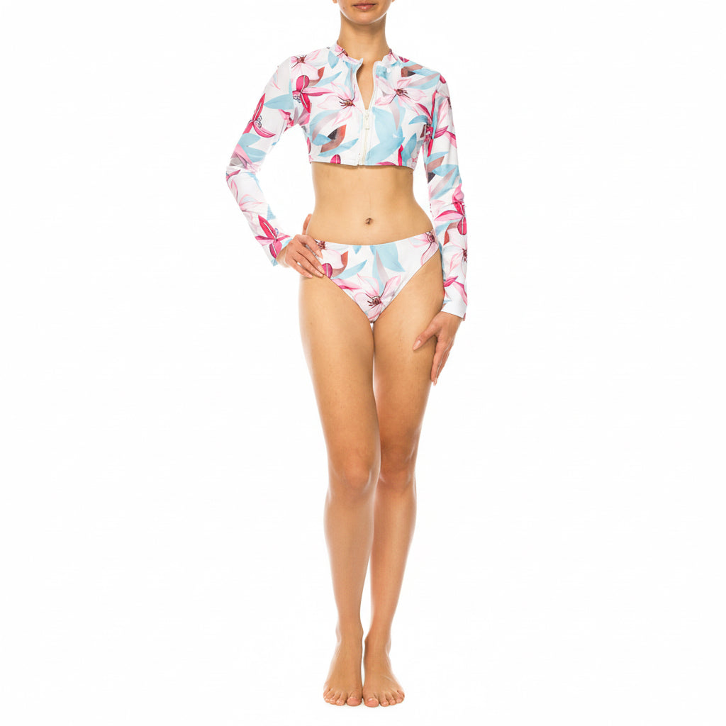 Bikini de dos piezas para mujer con manga larga y cierre frontal, estampado floral en tonos pastel, bottom clásico, modelo en estudio con fondo blanco.